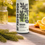 Sparklebuck Balsam sparkling buckwheat tea can on a wooden surface with greenery and oranges in the background.